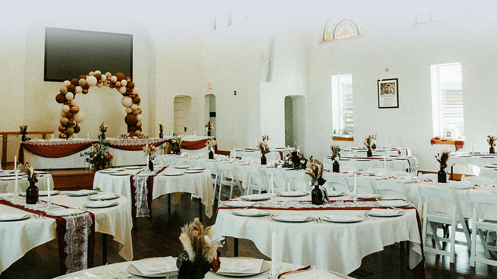 A beautifiul white linen banquet in the main chapel room, with round tables and white chairs.