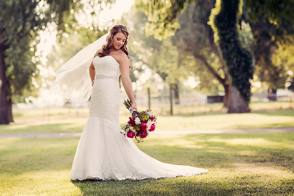 A bride poses, looking down over her shoulder, as she stands in between the tall trees