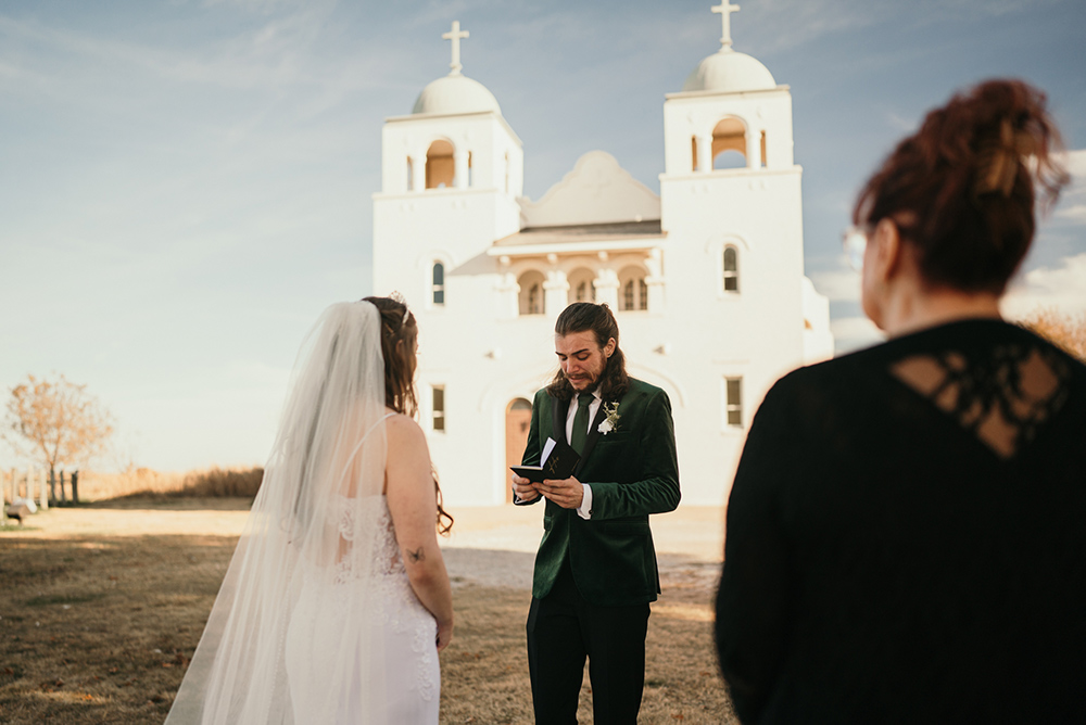 A groom reads from a small notebook to his bride
