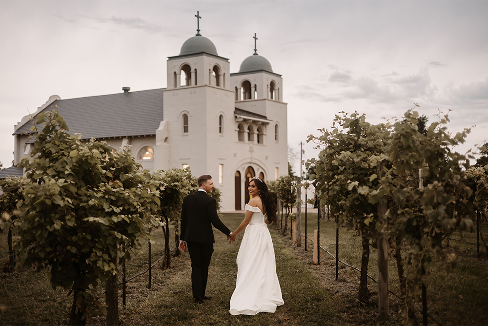 A happy couple, holding hands while walking through the vineyard
