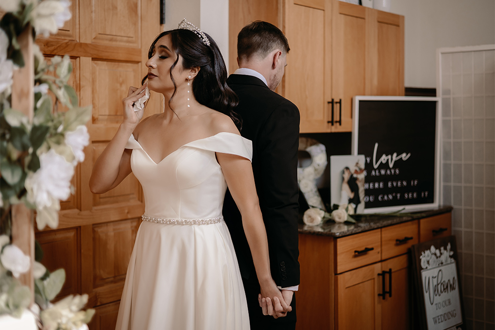 Bride and groom stand back to back, taking the moment in, while in one of the prep rooms